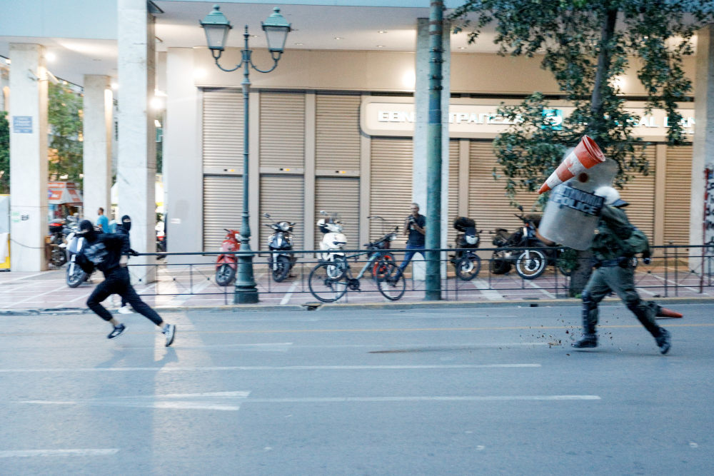 Διαδηλωτής τρέχει μπροστά από άνδρα των ΜΑΤ στη Σταδίου