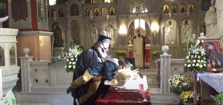 Priest lifts a small child to kiss the clothes of the late Metropolitan Langadas