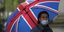 Άνδρας με ομπρέλα στα χρώματα της Βρετανίας και μάσκα προστασίας από τον κορωνοϊό