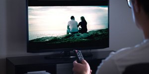Άνδρας με τηλεκοντρόλ μπροστά από ανοιχτή τηλεόραση